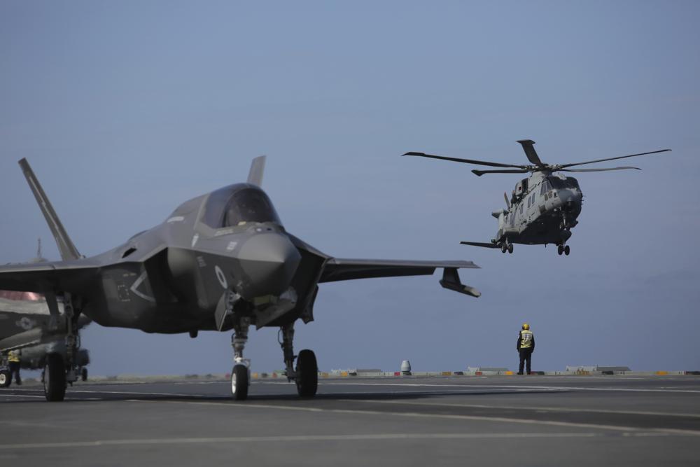 Military personnel direct F35 jets and helicopters on the deck of the